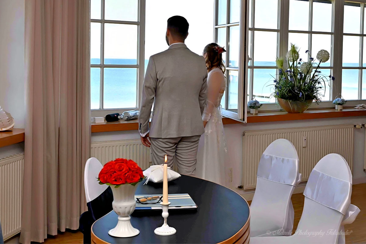 Ein stiller Moment voller Emotion: Direkt nach der Trauung blickt das frisch vermählte Paar aus dem Fenster des Standesamts in Zingst auf das weite Meer. Die Ostsee zeigt sich ruhig und klar, als würde sie die neue Verbindung segnen. Diese intime Szene wurde vom Mazelle Photography Fotostudio® aus Dranske kunstvoll eingefangen – ein Symbol für den Beginn eines gemeinsamen Lebenswegs inmitten der Naturkulisse des Fischland-Darß.