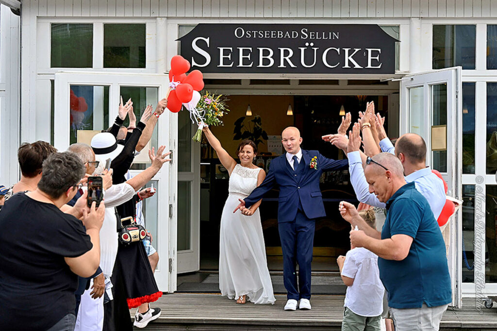 Das frisch vermählte Hochzeitspaar verlässt den historischen Trausaal der Seebrücke Sellin und wird von Familie und Freunden im liebevoll gestalteten Spalier empfangen. Die Ostsee im Hintergrund, das Lichtspiel auf dem Wasser und die emotionale Atmosphäre machen diesen Moment einzigartig. Fotografisch begleitet vom Hochzeitsfotografen des Mazelle Photography Fotostudio® – mit Feingefühl und künstlerischem Blick eingefangen.