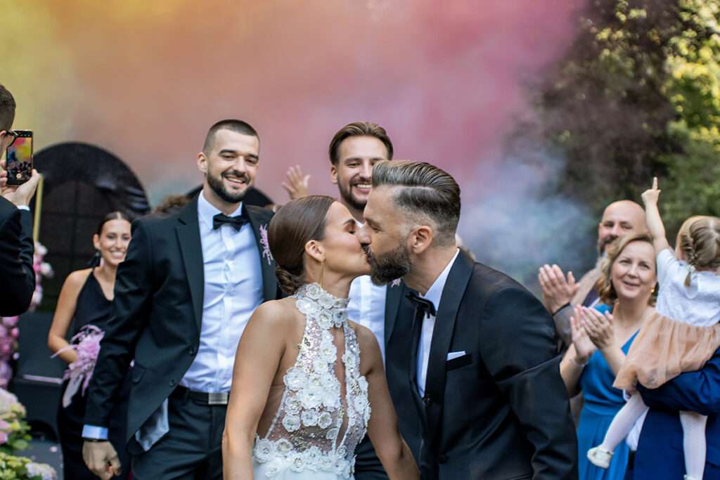 Ein Moment voller Emotionen: Direkt nach dem Ringtausch küsst sich das Brautpaar, während im Hintergrund ein Feuerwerk den Himmel über dem Schlosspark Borowa in Polen erleuchtet.