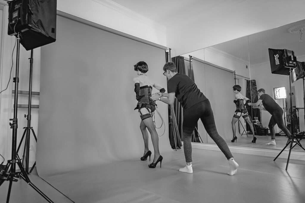 Dieses Bild zeigt einen seltenen Blick hinter die Kulissen im Ballettstudio in Warschau. Fotografin Magdalena Mazelle unterstützt das Model beim Anziehen, während Fotograf Andreas Mazelle diesen Moment respektvoll aus der Distanz dokumentiert.